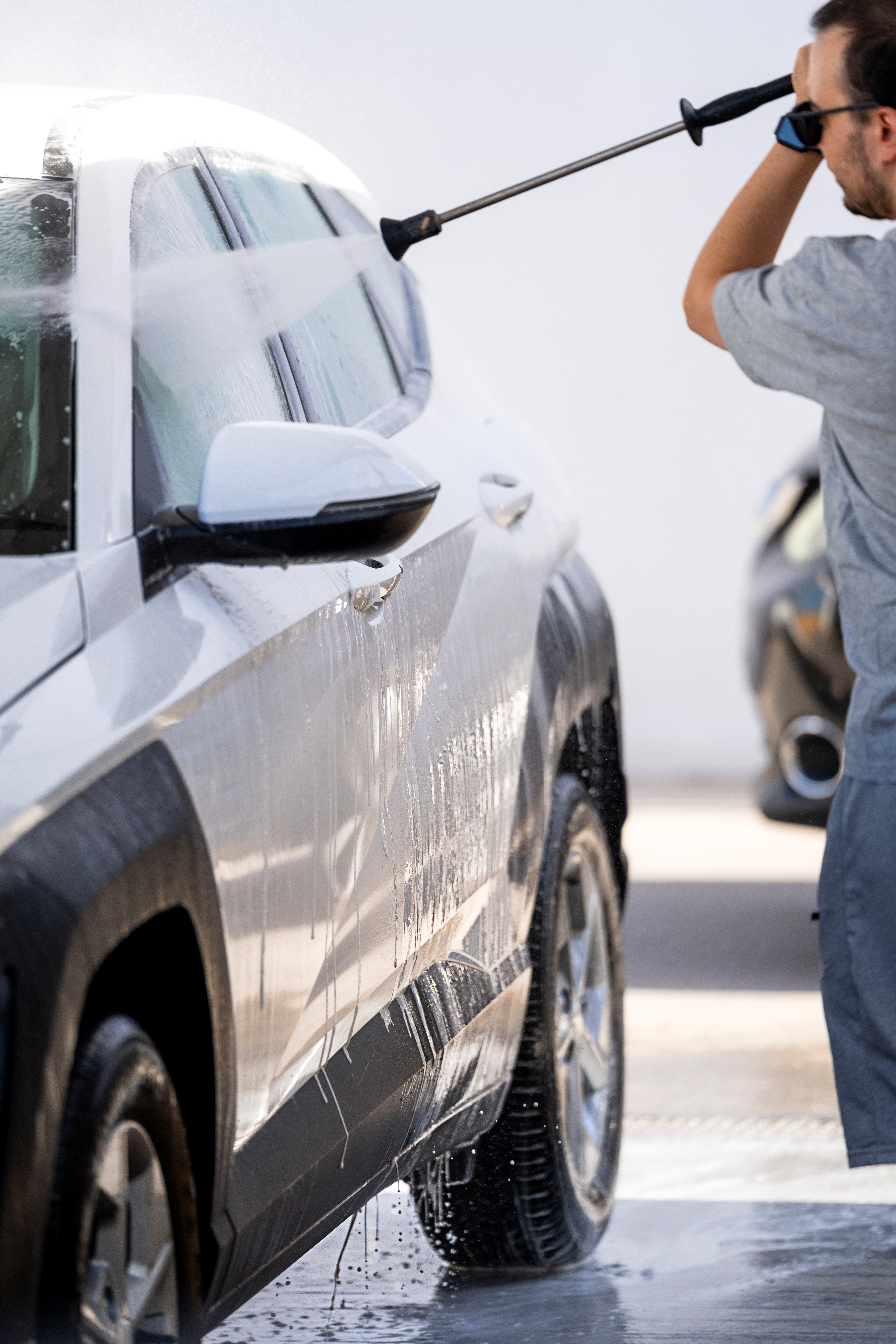 Man using a high-pressure hose to clean white vehicle at car wash facility